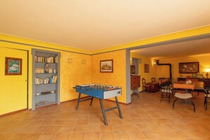Ein Zimmer mit einem Kicker, einem Bücherregal, einem Esstisch mit Stühlen und einem Bild an der Wand.