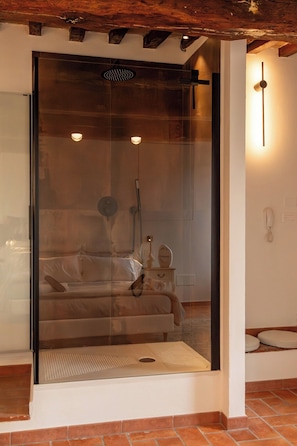 A room with a glass shower enclosure, a bed, a bedside table, and a wall-mounted telephone.