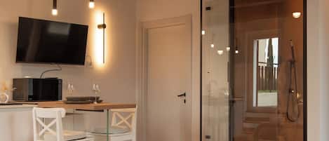 A bedroom with a bed, a desk with a TV, a shower, and a glass door leading to a balcony.