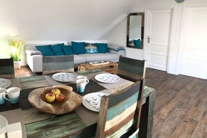 A dining area with a wooden table, chairs, and a white sofa with teal cushions. - Anchorage (To the old coach house Norddeich) (Norddeich)