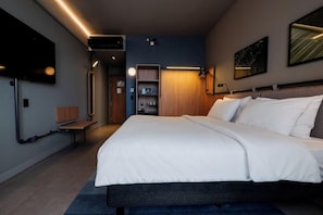 Una habitación de hotel moderna con una cama grande, un televisor de pantalla plana en la pared y un banco empotrado.