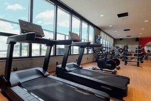 Un gimnasio con cintas de correr, máquinas de pesas y un ventanal grande.