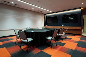 Un salón de conferencias con una pantalla grande, mesas redondas y sillas.