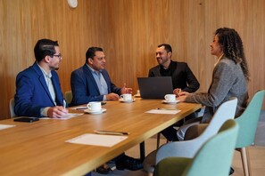 Una sala de conferencias con una mesa de madera, cuatro personas participando en una discusión y un portátil sobre la mesa.