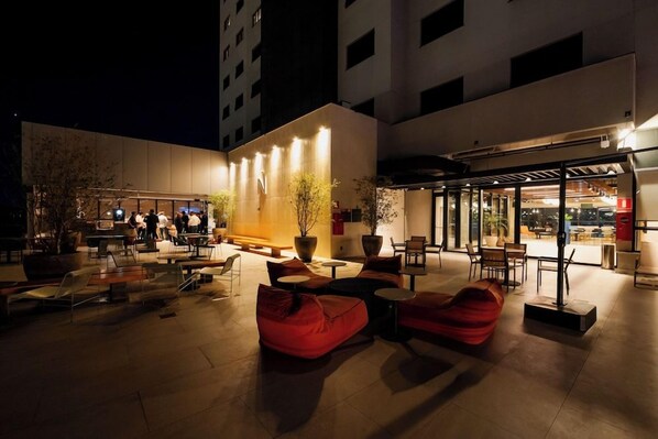 An outdoor seating area with tables and chairs, a covered seating area, and a building entrance with a sign. - Novotel Uberlandia (Uberlandia)