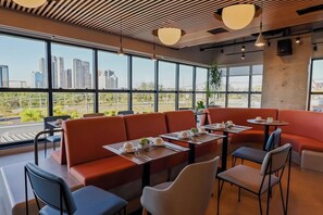 Un restaurante moderno con amplios ventanales, asientos rojos y vistas a la ciudad.