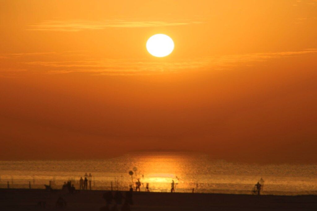 A sunset over a beach with silhouettes of people and a calm sea.