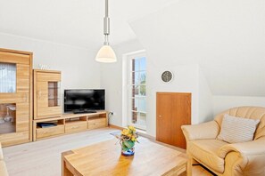Ein modernes Wohnzimmer mit Fernseher, Holzmöbeln, einem Couchtisch mit einer Vase und einem Ledersofa.