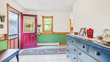 A room with a red door, a window with a view of trees, a blue dresser, and a patterned rug.