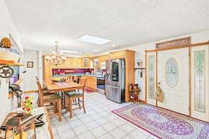 A spacious kitchen with wooden cabinets, a stainless steel refrigerator, and a dining area with a table and chairs. - Little Camp Christmas (Plattsburgh)