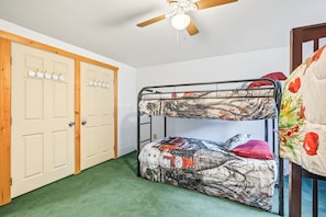 A bunk bed with a camouflage-patterned bedding, a ceiling fan, and a wooden door with a light switch. - Little Camp Christmas (Plattsburgh)