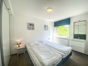 A bedroom with two beds, a nightstand, a window with a view, and a mirror. - Ok38 Holiday Home With dog (Grijpskerke)