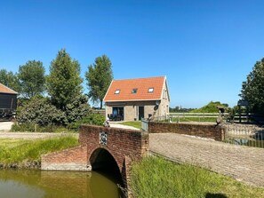 A brick house with a red roof, a small bridge, and a pond. - Ok38 Holiday Home With dog (Grijpskerke)