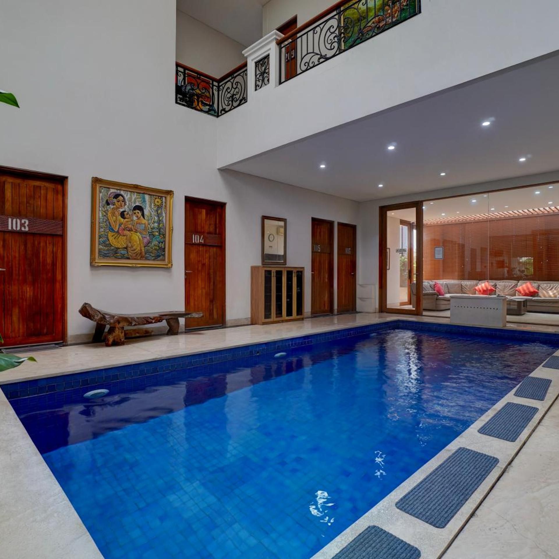 Una piscina con un banco de madera, un mural y un ventanal que da a una zona de estar.
