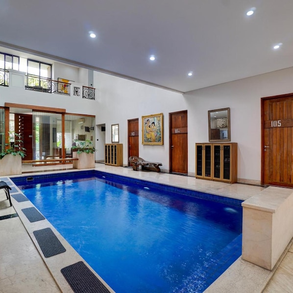 A swimming pool with a tiled deck, wooden doors, and a bench. - Collection O Near Universitas Pelita Harapan Formerly Ohana Residence Karawaci (Curug)