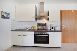 A compact kitchen with white cabinets, a stove, an oven, and a coffee maker. - Holiday apartment with 1 bedroom (Ostseebad Prerow)