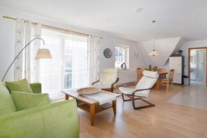 A spacious living area with a green sofa, wooden coffee table, and a dining table with chairs. - Holiday apartment with 1 bedroom (Ostseebad Prerow)