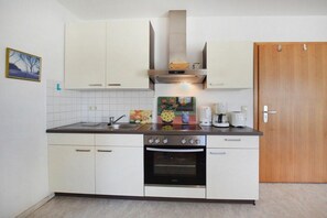 Eine Küche mit weißen Schränken, einem Herd, einem Backofen, einer Spüle und einer Holztür.