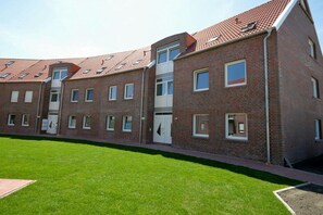 Un immeuble résidentiel à plusieurs étages, doté d’une façade en briques, de nombreuses fenêtres et d’un toit plat équipé de panneaux solaires.