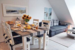 A dining area with a table set for breakfast, a sofa, and a view of the outdoors. - Frisian happiness on the dike (Norddeich)