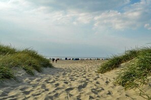 A sandy beach path with dunes on either side, leading to a distant shoreline with people and beachgoers. - Frisian happiness on the dike (Norddeich)