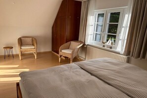 Ein Schlafzimmer mit zwei Einzelbetten, einem Holzschrank, einem Korbstuhl und einem Fenster mit Vorhängen.