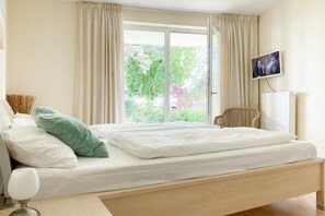 Une chambre à coucher avec un lit, un téléviseur fixé au mur et une fenêtre avec des rideaux.