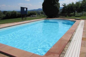 A rectangular swimming pool with clear blue water, surrounded by a tiled deck and a grassy area with trees and a mountain in the background. - Holiday home with 3 bedrooms (St. Stefan ob Stainz)