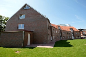 A multi-story brick building with a sloped roof, a covered entrance, and a paved pathway leading to the entrance. - Holiday apartment with 2 bedrooms (Norddeich)