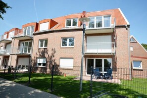 A multi-story residential building with a brick facade, balconies, and a fenced outdoor area with seating. - Holiday apartment with 2 bedrooms (Norddeich)
