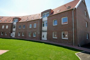 Une rangée d’immeubles en briques, dotés de nombreuses fenêtres et portes, avec un toit plat et une pelouse bien entretenue à l’avant.