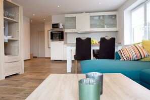 A modern kitchen with white cabinets, a microwave, and a dining area with a table and chairs. - Holiday apartment with 2 bedrooms (Norddeich)