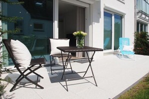 An outdoor seating area with a table and two chairs, a blue lounge chair, and a potted plant. - Timmare IV Little Crab (Timmendorfer Strand)