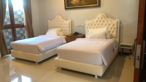 A hotel room with two beds, a nightstand, and a painting on the wall. - Pesona Osing Hotel Butik (Genteng)