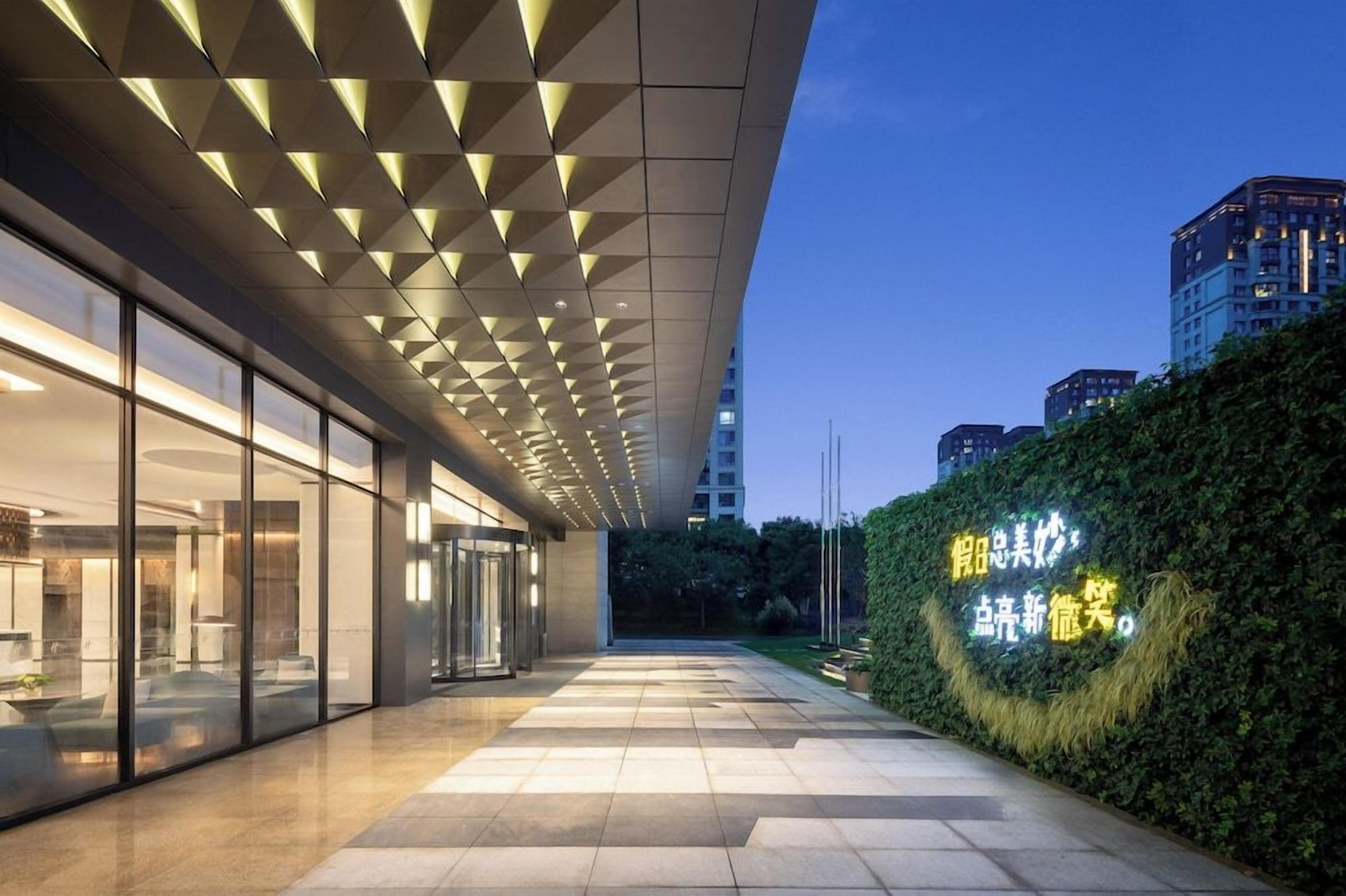 A modern building with a glass facade, a geometric ceiling design, and a well-lit entrance area.