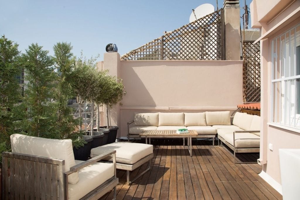 An outdoor patio with a wooden deck, a white sofa, and a small table.