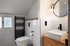 A bathroom with a white toilet, a black towel rack, a white sink with a wooden countertop, and a mirror with a gold frame.