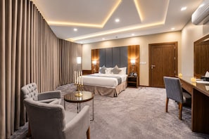 A hotel room with a bed, a desk, a chair, a bedside table, and a wall-mounted TV.