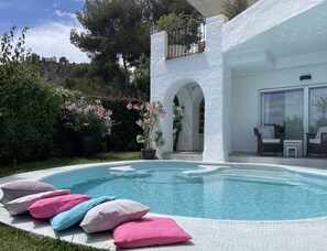 A swimming pool with a white exterior wall, a covered patio area with outdoor furniture, and a view of a mountainous landscape. - Holiday Apartment With 1 Bedroom (La Herradura-Marina Del Este Granada)