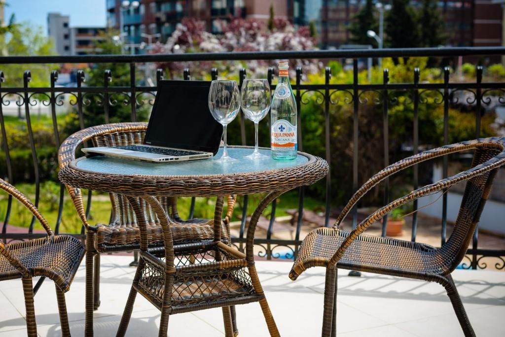 A wicker table with a laptop, two glasses, and a bottle of water on a balcony.