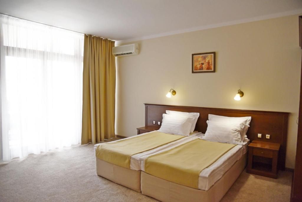 Ein Hotelzimmer mit einem Doppelbett, zwei Nachttischen, einer Lampe, einem Fenster mit Vorhängen, einer Klimaanlage und einer Wandleuchte.