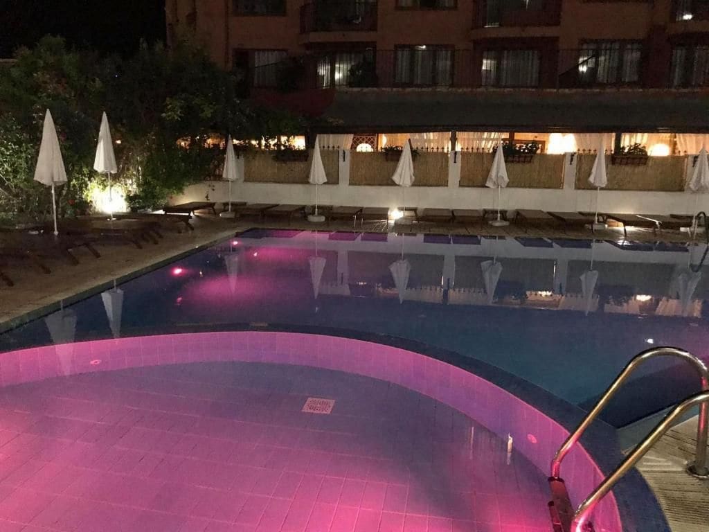 Una piscina de borde curvo, rodeada de sillas de descanso y sombrillas, con un edificio al fondo.