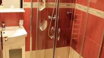 Une cabine de douche fermée par des parois en verre, avec un lavabo blanc et un miroir sur le côté gauche.