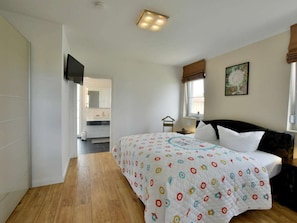 A bedroom with a bed, a nightstand, a window with curtains, a wall-mounted TV, and a bathroom visible through an open door. - Holiday Home With 3 Bedrooms (Trent)