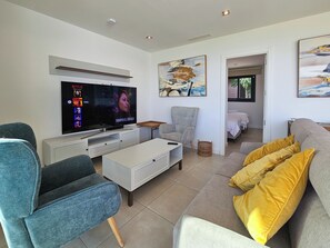 Ein modernes Wohnzimmer mit Flachbildfernseher, einem grauen Sofa, einem blauen Sessel und einem Couchtisch.