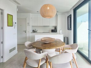 Une cuisine moderne avec des meubles blancs, une table ronde en bois entourée de chaises et un luminaire suspendu.