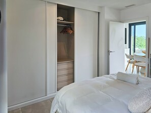 Ein Schlafzimmer mit Bett, einem Kleiderschrank mit Platz zum Aufhängen und Blick durch eine offene Tür.