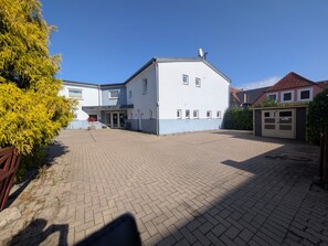 A two-story building with a paved courtyard, a satellite dish on the roof, and a small shed to the right. - Nordnest: Holiday apartment in the center of Kappeln with parking and bike shed (Kappeln)