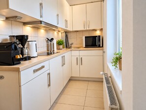 A modern kitchen with white cabinets, stainless steel appliances, and a window with a view. - Nordnest: Holiday apartment in the center of Kappeln with parking and bike shed (Kappeln)