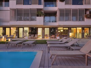 Ein Hotel mit Poolbereich, Liegestühlen und einer hell erleuchteten Lobby.